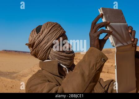 Tibesti, Tchad - 31/12/2012. Un jeune homme du Tchad prend une photo en utilisant un comprimé. Dans les dunes du Sahara. Banque D'Images