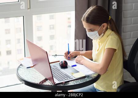 Fille dans le masque médical fait des devoirs en utilisant l'apprentissage à distance Banque D'Images