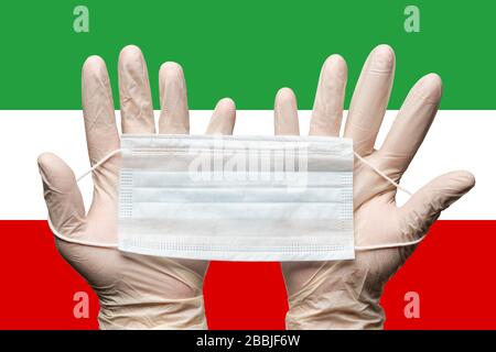 Le masque respiratoire paramédic est tenu à deux mains dans des gants médicaux blancs sur le drapeau de fond de la République islamique d'Iran. Concept coronavirus Banque D'Images