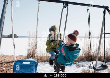 Enfants jouant sur une balançoire double ensemble au bord de l'océan en Suède Banque D'Images
