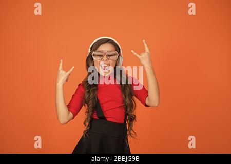 Piste froide. Événement et divertissement. Fille de fête. Accessoire de fête. Amuse-toi bien. Liste de lecture pour la fête. Concept de musique. Enfant porter des lunettes. Magasin de mode de lunettes. Fille avec lunettes arrière-plan orange. Banque D'Images