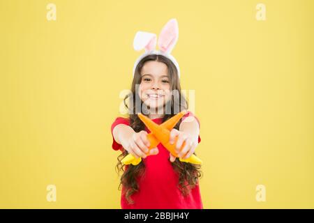 Un petit déjeuner sain. Bon pour vos dents. Grignotez des carottes comme du lièvre. Gamin dans les oreilles de lapin mangeant des carottes. Costume de lapin enfant avec carotte. Nourriture pour petite fille heureuse pour lapins. Enfance saine. Banque D'Images