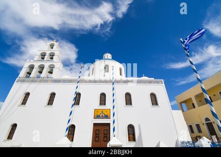 L'église de Panagia Platsani avec un drapeau grec volant dans le village perché d'Oia, sur l'île de Santorin, Grèce. Banque D'Images