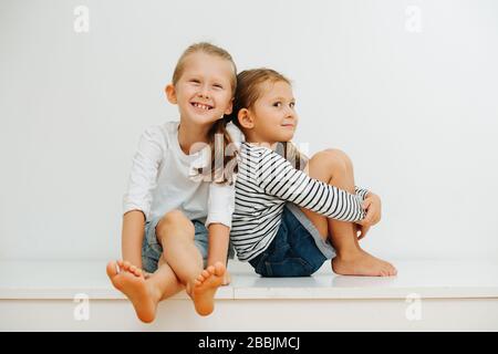 Sœur la penche sur son frère, alors qu'ils s'assoient sur une table. Sur un mur blanc Banque D'Images