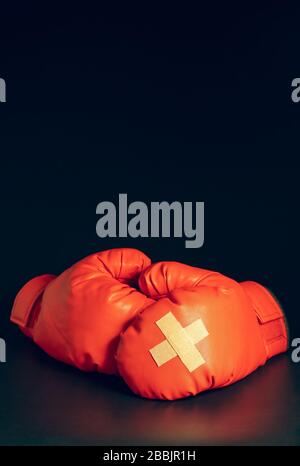 Gants de boxe rouge sur fond sombre. Plâtre adhésif l'un sur l'autre sur les gants de boxe. L'idée de faire mal ou de combattre la perte d'affaires riva Banque D'Images
