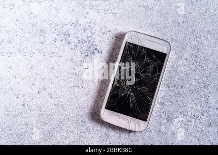 Téléphone portable plat cassé avec écran noir fissuré sur fond en béton. Banque D'Images