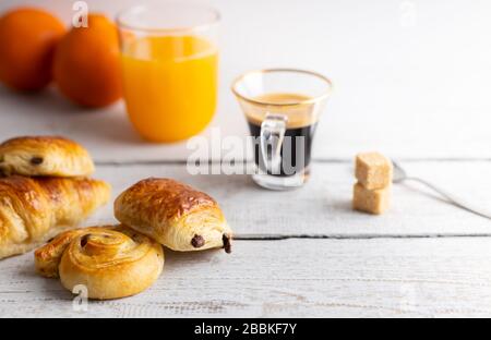 Petit-déjeuner avec croissants, petits pains à la cannelle et biscuits au chocolat, jus d'orange frais et café sur le côté sur fond blanc. Banque D'Images