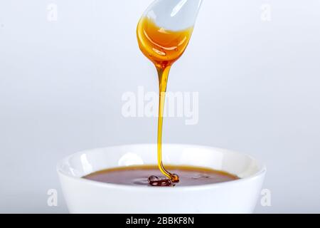 le miel s'écoule de la cuillère en céramique à la cuvette en céramique Banque D'Images