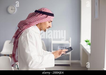 Arab man utilise une tablette pour travailler en ligne au bureau. Banque D'Images