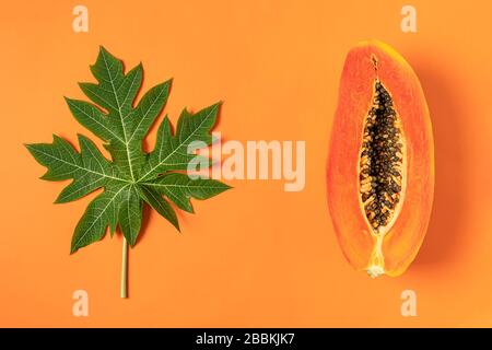 Fruits de papaye fraîchement coupés mûrs avec feuilles de papaye vertes sur fond orange, plat, espace de copie Banque D'Images