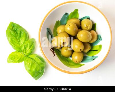 Un bol d'olives vertes dénoyautées et une branche de basilic sur une nappe blanche Banque D'Images