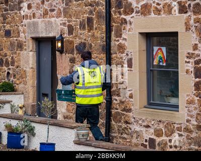 East Lothian, Ecosse, Royaume-Uni, 1 avril 2020. Livraisons locales de nourriture pendant la pandémie de Coronavirus de Covid-19: Yester Farm Dairies commence deux fois par semaine des livraisons gratuites de maison aux résidents de East Lothian. Yester secteur est une ferme familiale qui fournit des produits laitiers artisanaux primés. Ils ont été inondés de commandes. Photo: Dale, qui fait normalement du fromage à la laiterie fait les premières livraisons de lait à la maison à un steading rural avec un arc-en-ciel d'espoir dans la fenêtre Banque D'Images