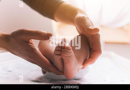 Pieds gros plan d'un nouveau-né. Le jeune père tient des pieds de bébé dans ses hiscans. Le petit bébé est allongé sur la table pour enfants . Il y a un enfant nouveau-né Banque D'Images