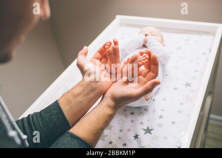 Pieds gros plan d'un nouveau-né. Le jeune père tient des pieds de bébé dans ses hiscans. Le petit bébé est allongé sur la table pour enfants . Il y a un enfant nouveau-né Banque D'Images