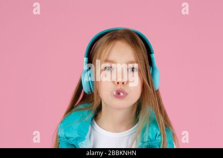 Une petite fille avec casque explose la gomme à mâcher rose sur un fond rose. Banque D'Images