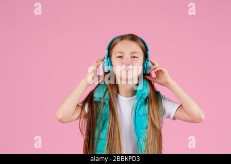 Une petite fille avec casque explose la gomme à mâcher rose sur un fond rose. Banque D'Images