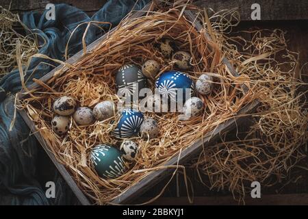 Œufs de caille et œufs de poulet colorés à la cire dans une boîte sur un foin. La composition de Pâques dans une ambiance sombre Banque D'Images
