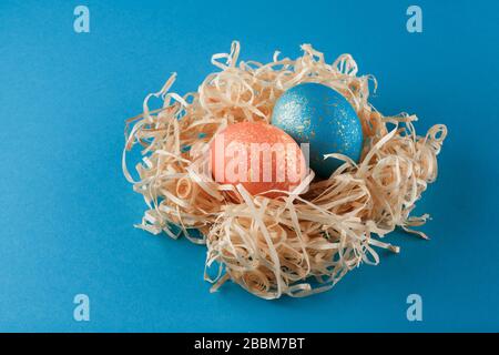 Les œufs de Pâques sont peints en bleu avec de l'or et de l'orange avec de l'or. Deux œufs se trouvent dans un nid de copeaux de bois. Œufs de pâques peints sur un fond bleu. Espace de copie. Banque D'Images