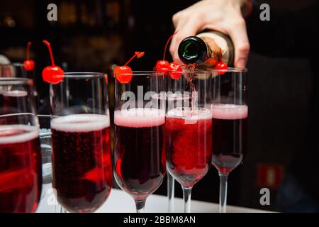 Le serveur verse du champagne dans les verres, qui se tiennent à la rangée. Sur le bord du verre est une cerise. Vin mousseux à une fête. Banque D'Images