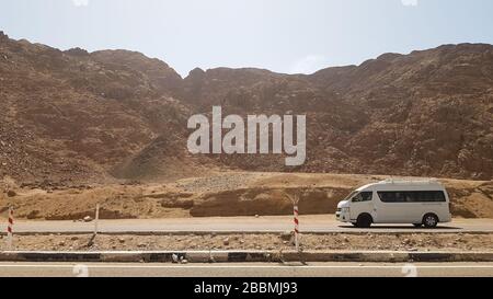 Egypte, Dahab - 17 octobre 2019: Un minibus de tourisme commercial blanc conduit avec les touristes sur une route d'asphalte dans le désert sur un fond de Banque D'Images