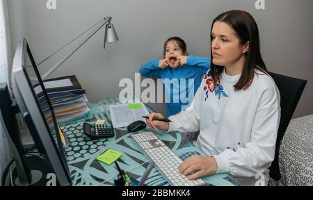 Femme télétravail en visioconférence avec sa fille qui grimace derrière elle Banque D'Images