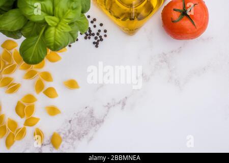 Séchez les pâtes, l'huile d'olive, la tomate, le basilic et le poivre noir sur un plan de travail en marbre blanc Banque D'Images