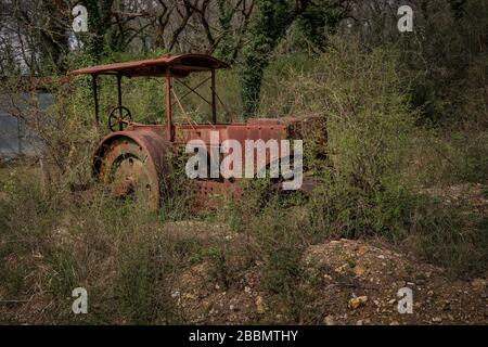 Un vieux tracteur abandonné à la rouille a déraillé garé dans une cour agricole dans l'herbe et les mauvaises herbes surcultivées Banque D'Images