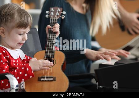 Bonne petite fille joue ukulele près des parents Banque D'Images