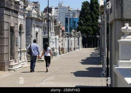 Homme et femme se tenant les mains en marchant dans les tombes bordant les rues étroites du cimetière de la Recoleta dans le centre de Buenos Aires Banque D'Images
