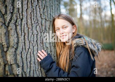 Une fille de 11 ans se penche sur le tronc d'un arbre énorme Banque D'Images