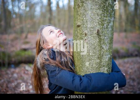 Une fille de 11 ans embrasse le tronc d'un petit arbre Banque D'Images