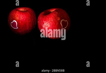 Autocollant en forme de coeur et gouttes d'eau sur une surface brillante de pomme rouge fraîche sur fond noir Banque D'Images