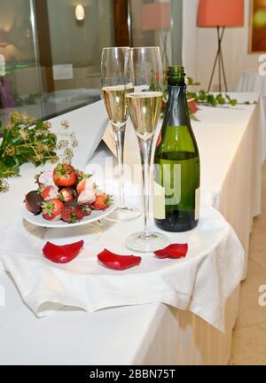Bouteille de champagne, deux verres et fraises au chocolat sur un plateau avec pétales de rose Banque D'Images