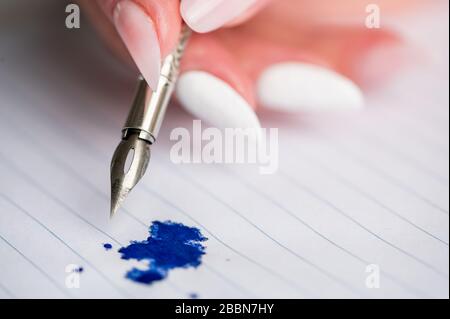 stylo à encre vintage dans la main femelle, tache d'encre bleue sur une feuille de papier Banque D'Images