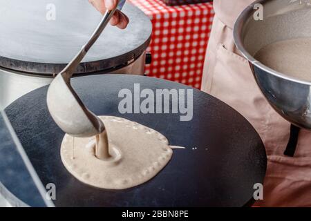 Faire des crêpes crêpes à un marché alimentaire. Une main verse de la pâte sur une grille métallique à l'extérieur Banque D'Images