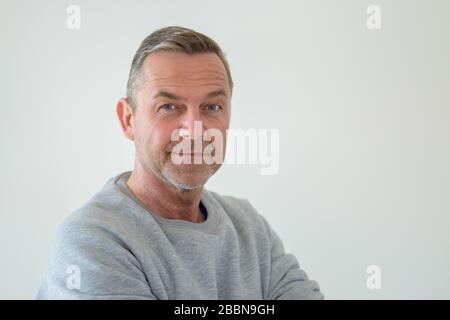 Portrait demi-tour de buste de l'homme d'âge moyen en pull gris, regardant l'appareil photo avec un sourire Banque D'Images