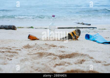 Bouteilles et chaussures enterrées dans la plage de sable blanc d'une rive de l'océan Banque D'Images