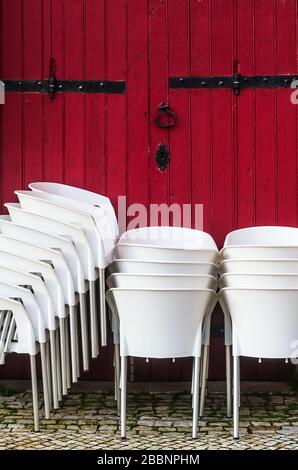 Des groupes de chaises blanches sont empilés contre une porte en bois rouge Banque D'Images