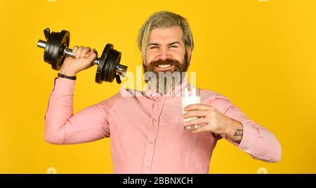 Quantité de graisse. Vitamines pour les muscles. Le sportif tient un haltère et un verre de lait. Régime protéique. Cocktail de protéines. Source de calcium. L'homme barbu boit du lait. Exercice dans la salle de sport. Lait bons nutriments. Banque D'Images