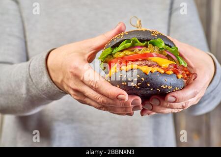 Les mains des femmes tiennent un hamburger noir Banque D'Images