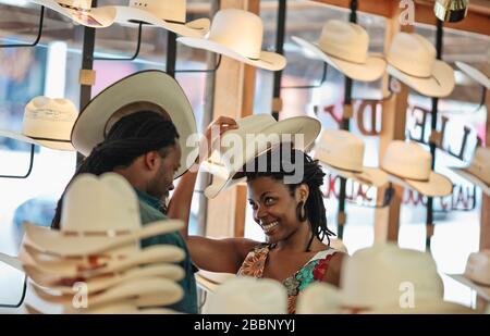 Un jeune couple heureux s'amuse à essayer sur des chapeaux de cowboy dans une boutique de chapeaux. Banque D'Images