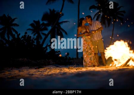 Mid-adult couple debout à côté d'un feu sur une plage. Banque D'Images