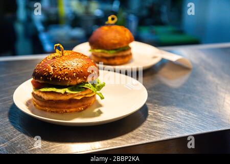 Plats prêts hamburgers au comptoir pour la livraison aux serveurs dans un restaurant et une cuisine en arrière-plan Banque D'Images