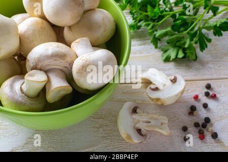 Champagnes frais crus entiers dans un bol vert près d'un bouquet de persil sur une table en bois. Champignons en tant que protéines végétales, alimentation alimentaire brute, végétarisme. Banque D'Images