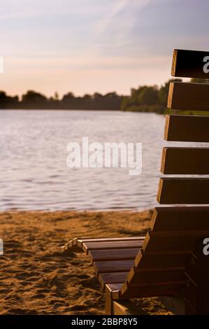 Scène idyllique et significative sur la plage avec vue sur un lac contre le soleil, un banc en bois au premier plan et une plage de sable dans le soleil du soir se réveillent Banque D'Images