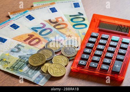 Billets et pièces de monnaie en espèces en euros avec une calculatrice rouge exprimant des thèmes financiers Banque D'Images