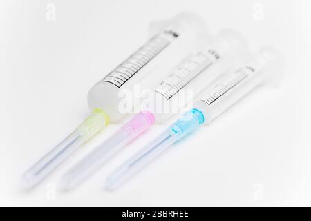 Trois seringues de différentes tailles, une couleur sur fond blanc utilisée comme équipement médical - mise au point sélective Banque D'Images