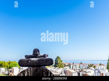 Sculpture du crâne et deux os à Cemitério do Alto de São João avec mausolées et paysage urbain sur fond. Banque D'Images