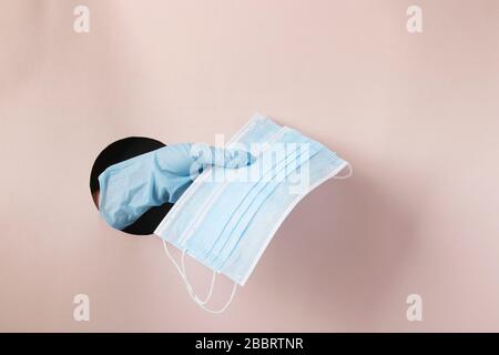 La main féminine dans un gant contient deux masques médicaux de protection par un trou rond en papier rose Banque D'Images