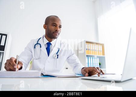 Photo de la famille doc peau sombre gars professionnel réussi écrire des prescriptions patients journal de base utiliser des statistiques en ligne bloc-notes portent blanc blouse de laboratoire Banque D'Images